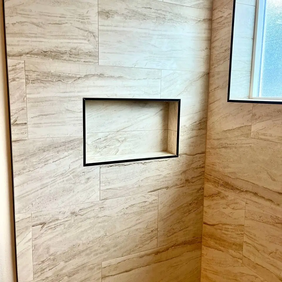 Vein-cut stone-look shower wall with a black-trimmed niche, tiled window return and corner ledge
