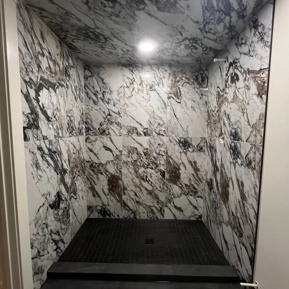 Walk-in shower clad floor to ceiling in bold black-veined marble-look tile with a black mosaic floor
