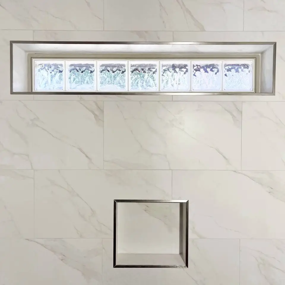 Marble-look shower wall with a metal-trimmed glass-block window recess above a matching niche