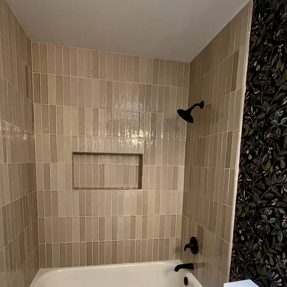 Tub surround in glossy taupe vertical tile with a tiled niche and matte black fixtures
