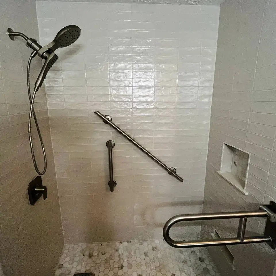 Shower in glossy white handmade-look tile with grab bars, a fold-up rail, a recessed niche and a hexagon marble floor