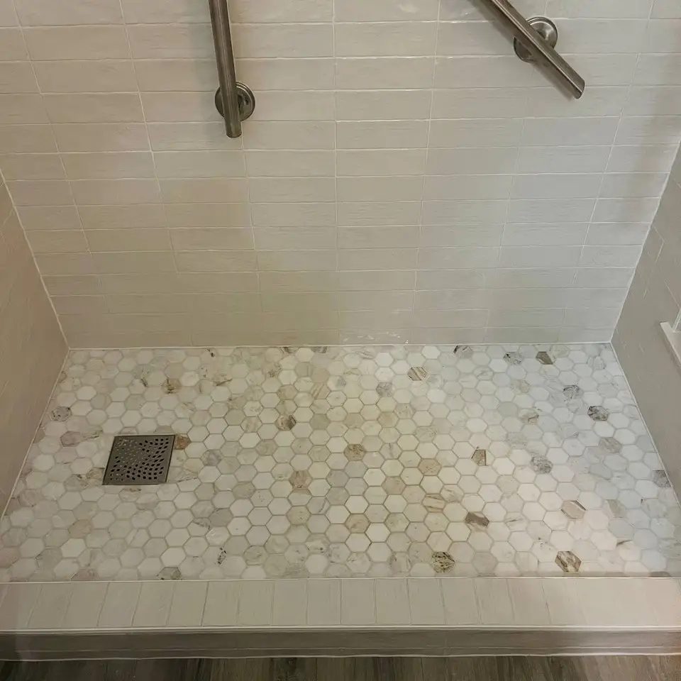 Hexagon mosaic shower floor with a square drain and tiled curb below glossy white wall tile