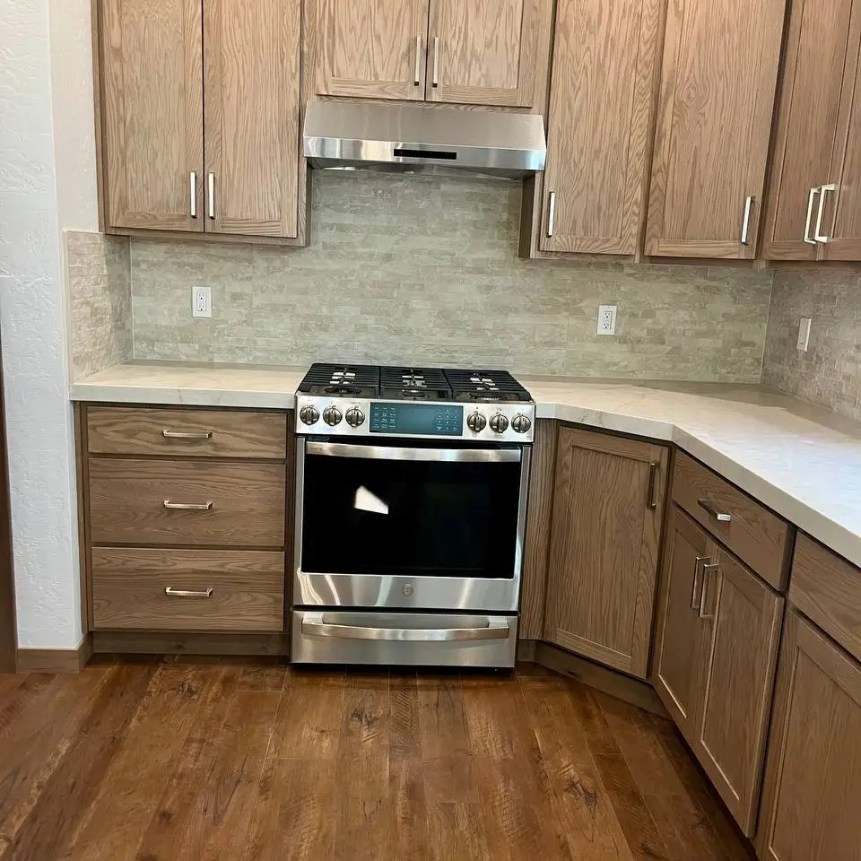 Kitchen with a stacked stone-look tile backsplash under oak cabinets, above wood-look plank flooring