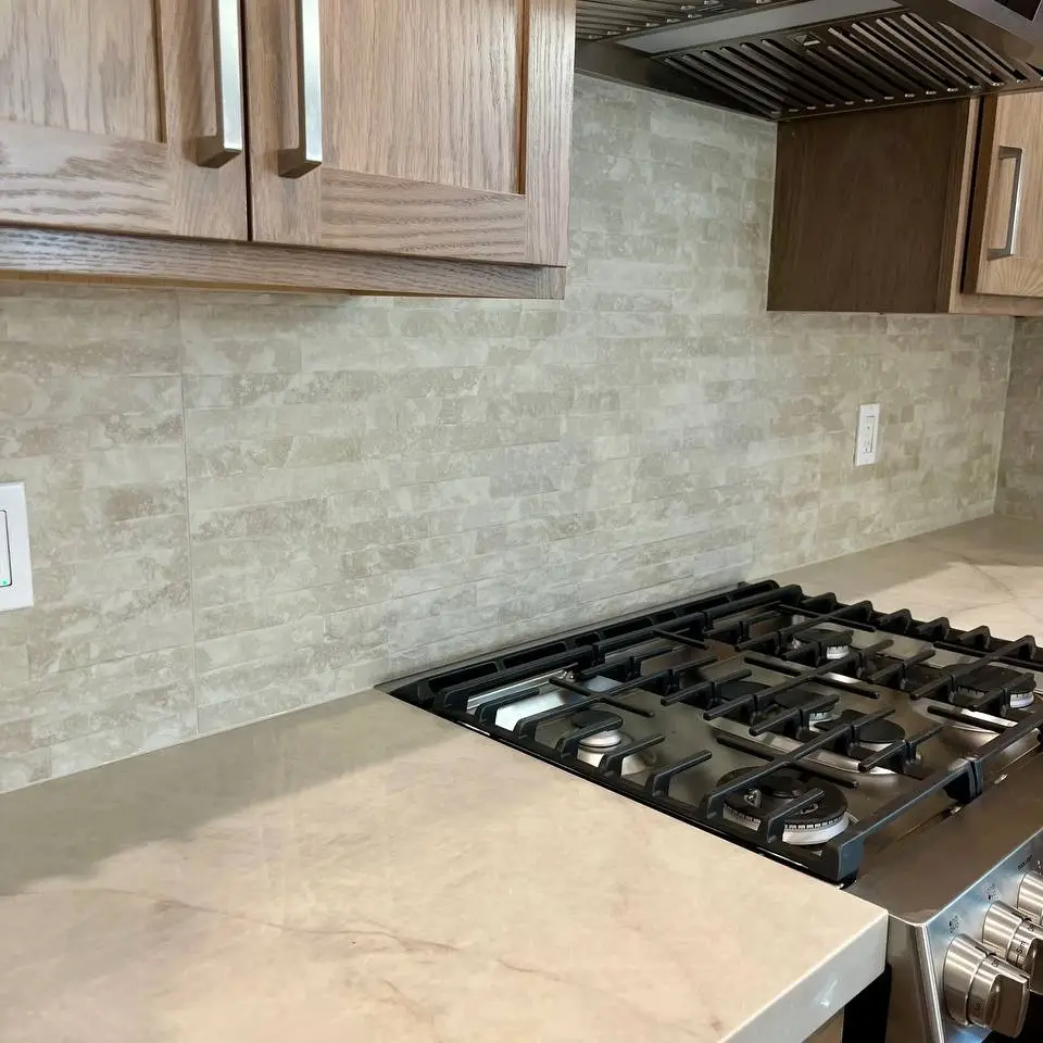 Stacked stone-look tile backsplash behind a gas range, between oak cabinets and a marble-look counter
