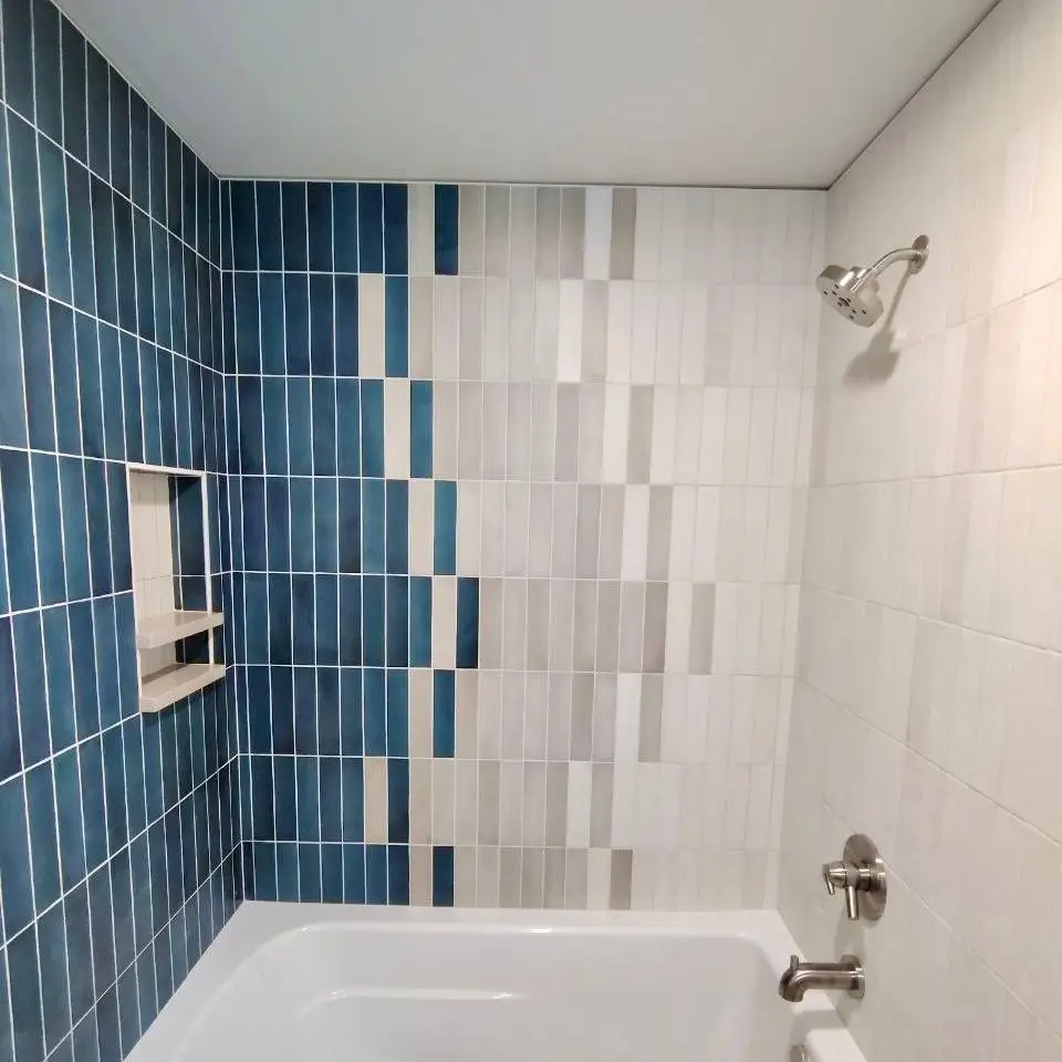 Tub surround in vertical stacked tile stepping from deep teal to cream, with a two-shelf niche