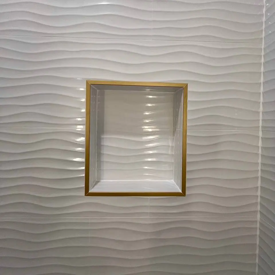 White wave-textured wall tile around a recessed niche framed in gold metal trim