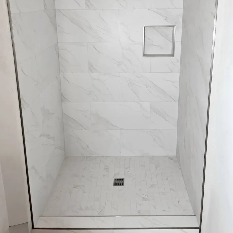 Walk-in shower in white marble-look tile with a metal-trimmed niche, mosaic floor and square drain